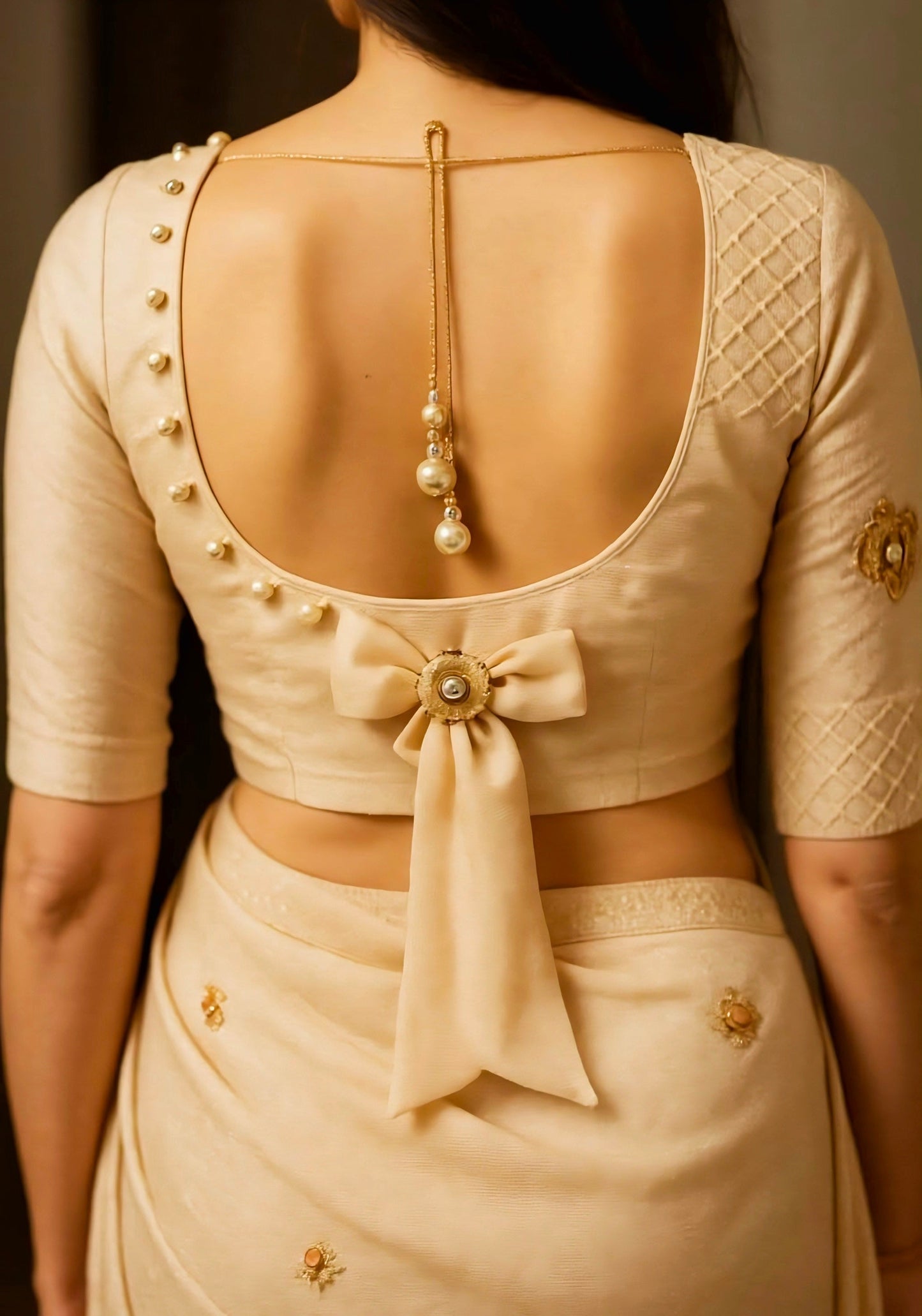Elegant cream silk blouse with pearl detailing, deep U-back design, and large satin bow accent.