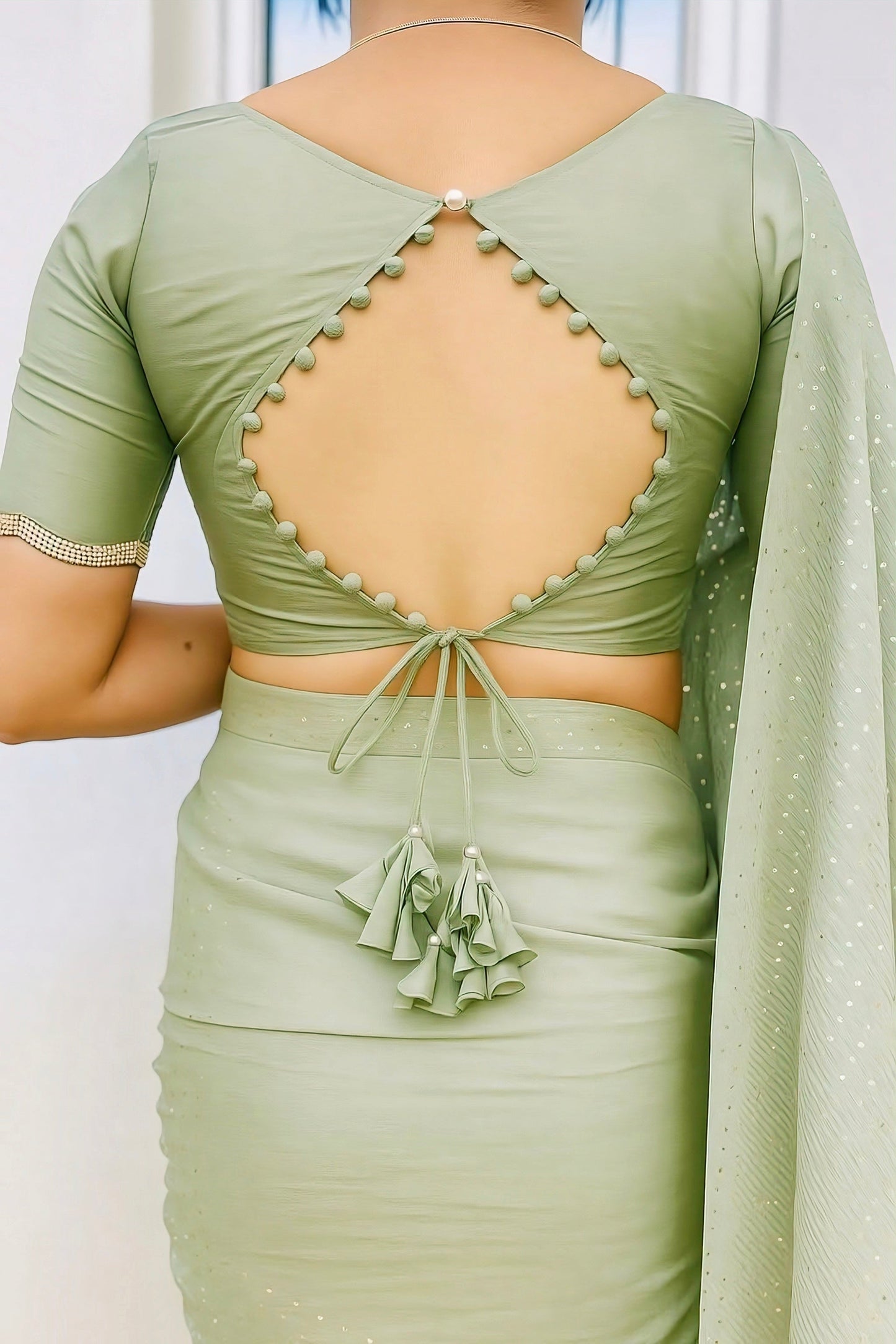 Pastel green blouse with diamond-shaped open back, pearl button closure, and tassel dori design for festive and wedding sarees.