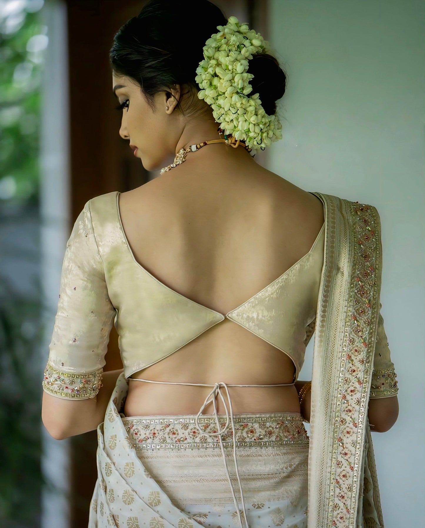 Cream silk blouse with deep V-cut back neck and tie-up design, perfect for elegant traditional saree looks.