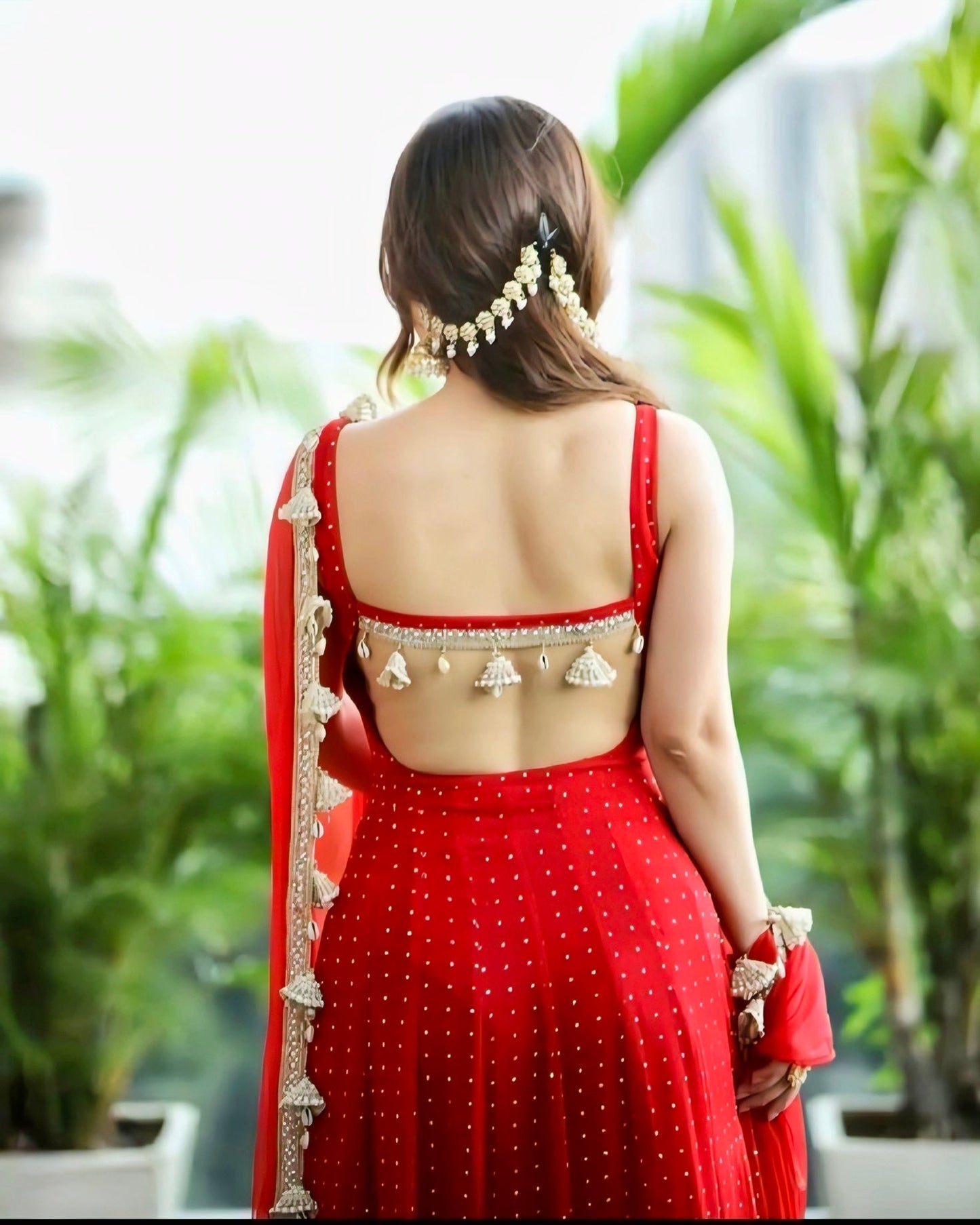Red backless blouse with pearl tassel detailing paired with a red embellished lehenga – festive ethnic outfit.