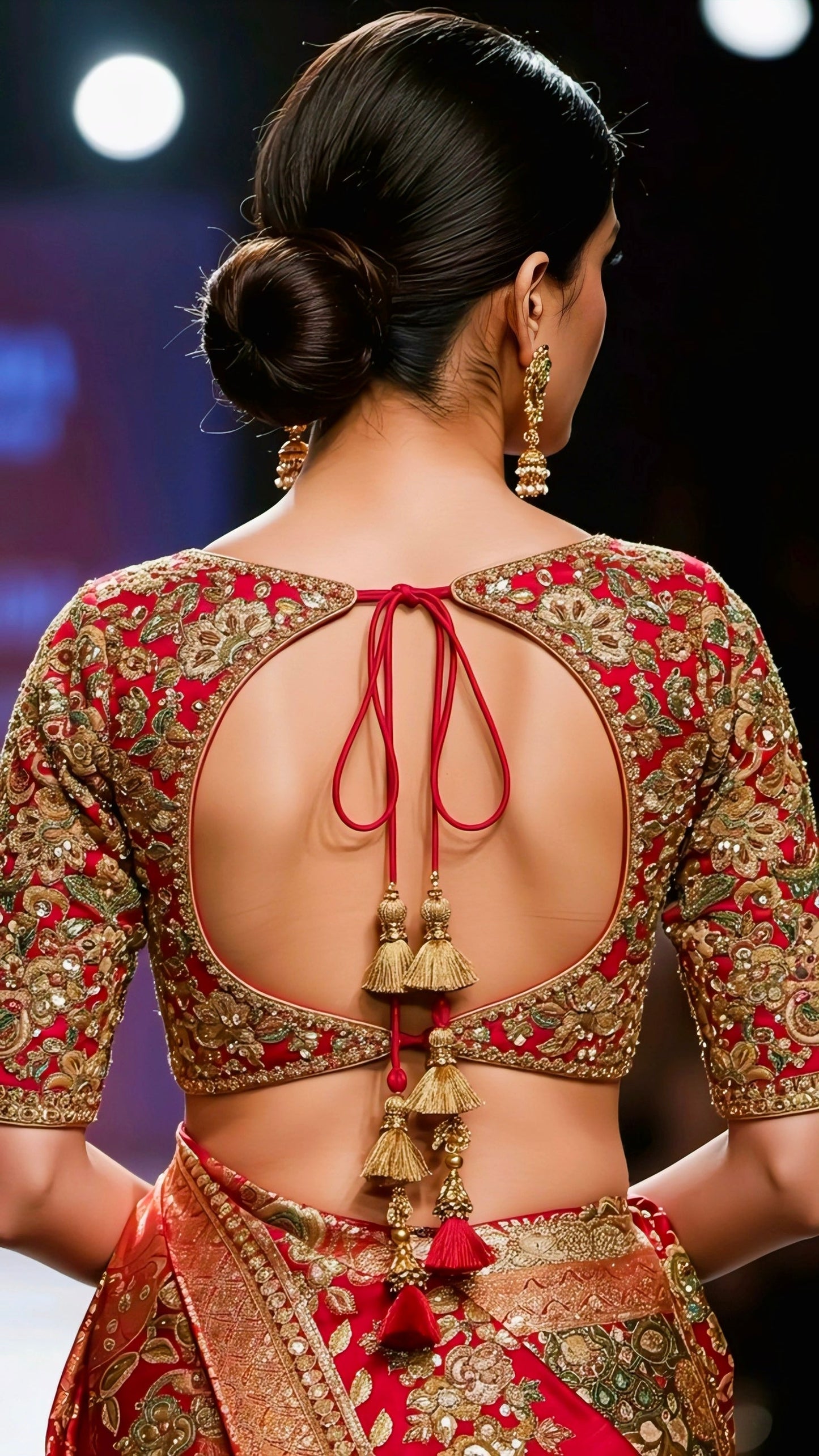 Woman wearing a red embroidered backless blouse with golden zari work and tassel dori tie-up, paired with a matching saree.