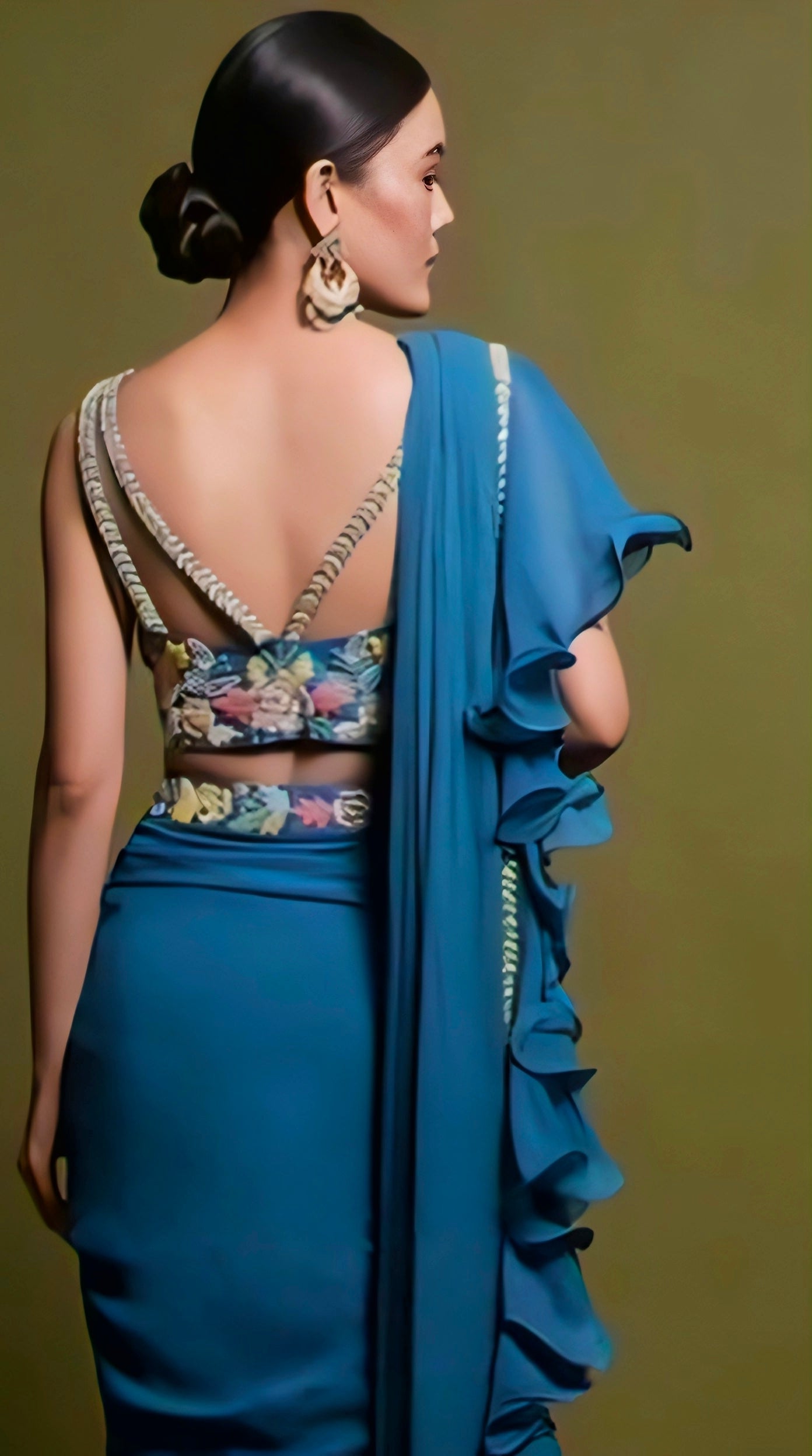 Woman wearing teal blue V-back floral embroidered blouse with ruffle saree — modern and elegant ethnic look.