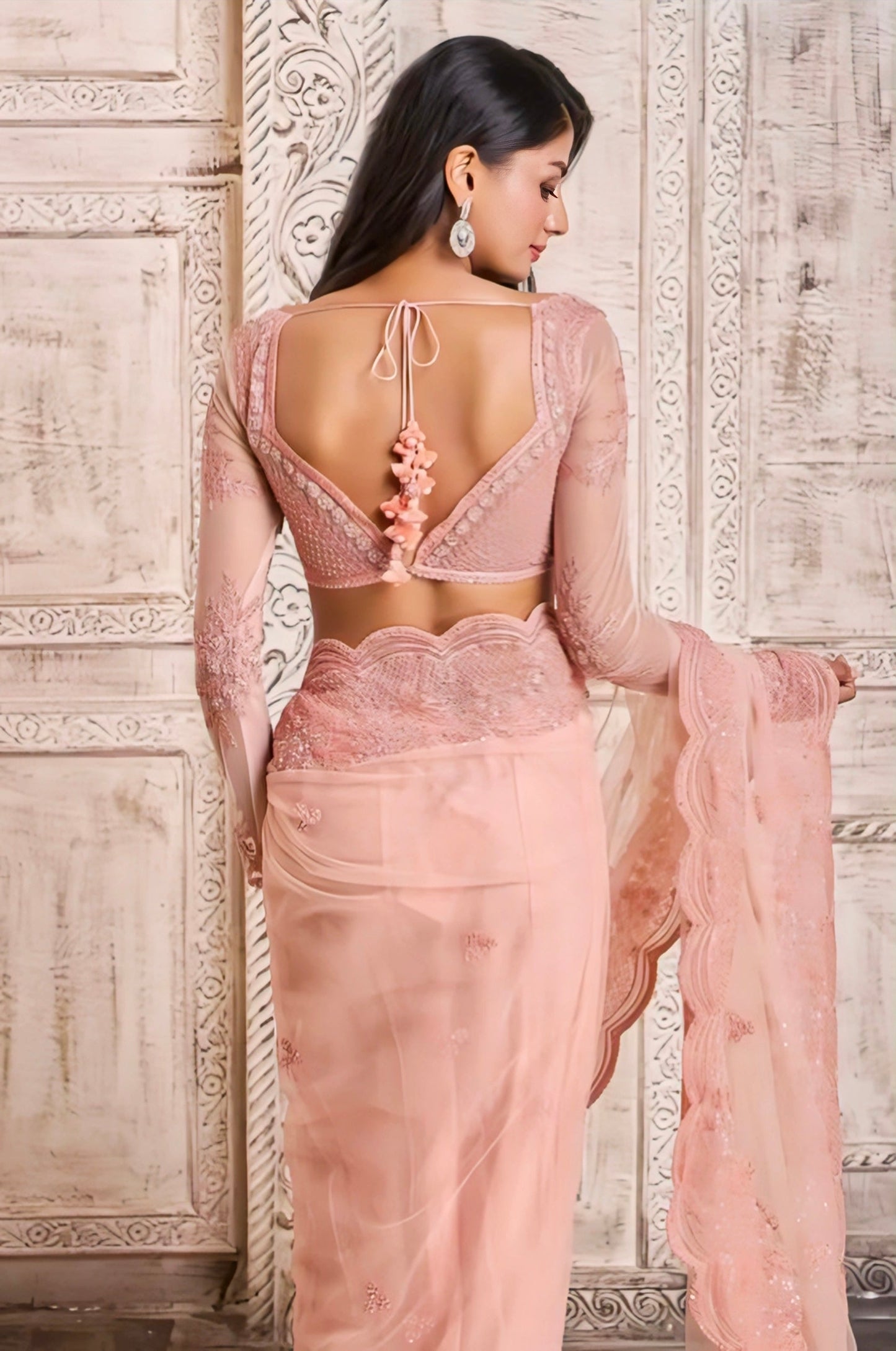 Woman wearing an elegant peach net saree blouse with full embroidered sleeves and deep back tie dori tassel design, perfect for wedding or festive look.