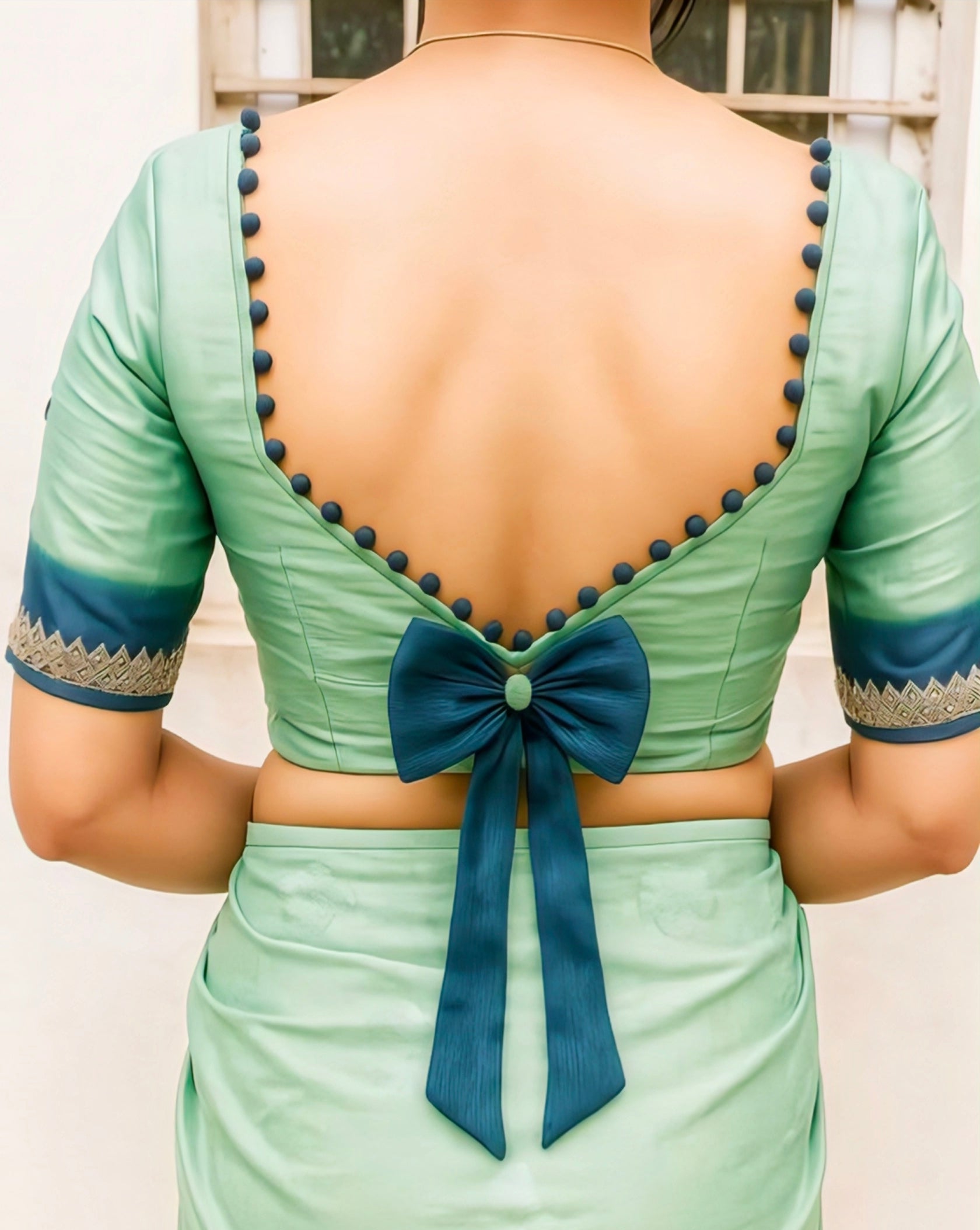 Mint green silk blouse with navy blue bow and button detailing on the deep V-back, perfect for festive and wedding saree looks.