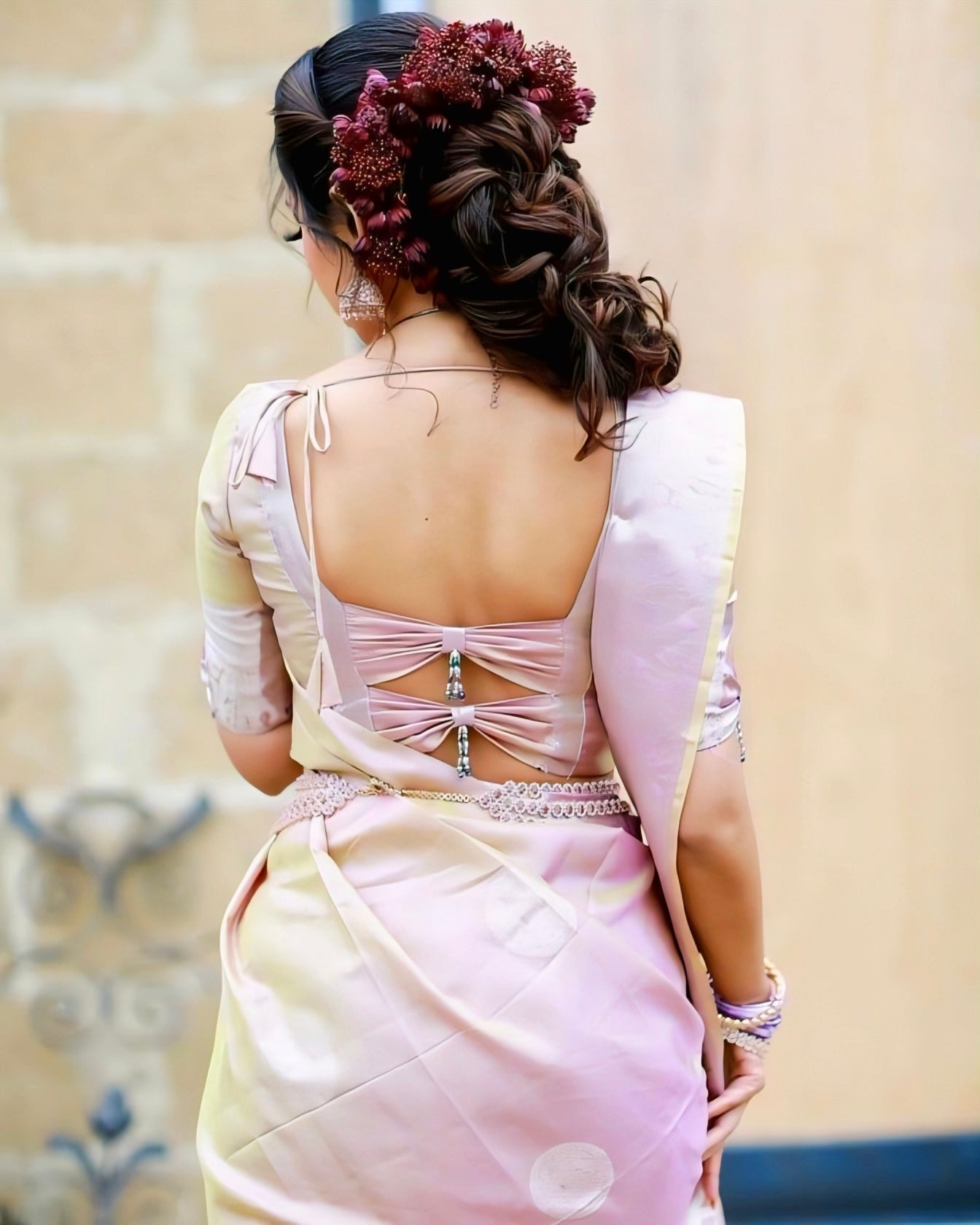 Pastel pink satin blouse with bow-back design and bead embellishment, paired with a soft saree — perfect for bridal and festive occasions.