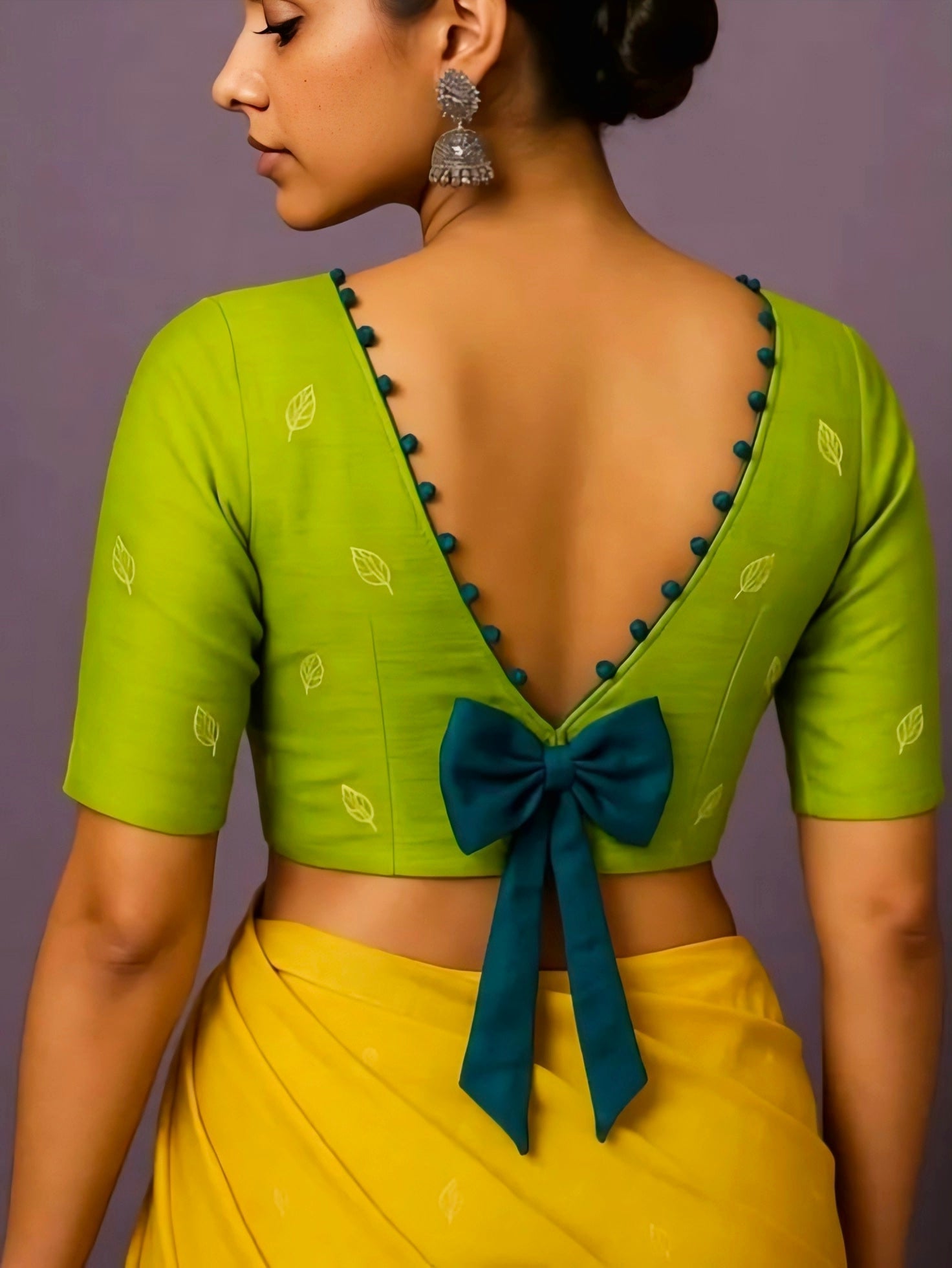 Woman wearing a green blouse with a blue bow and yellow saree against a purple background