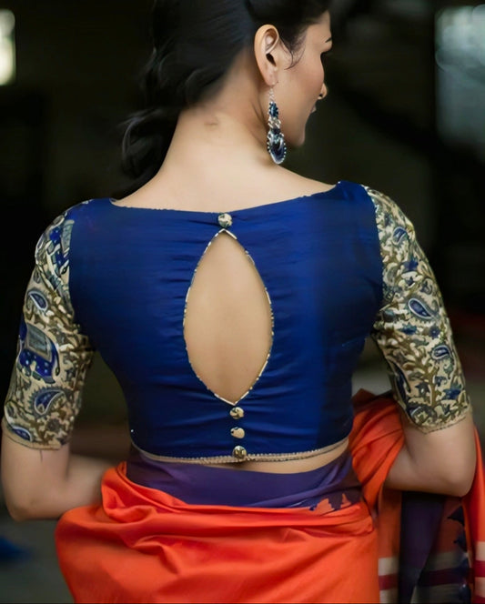 Woman wearing a blue blouse with a cut-out design and orange saree, back view.