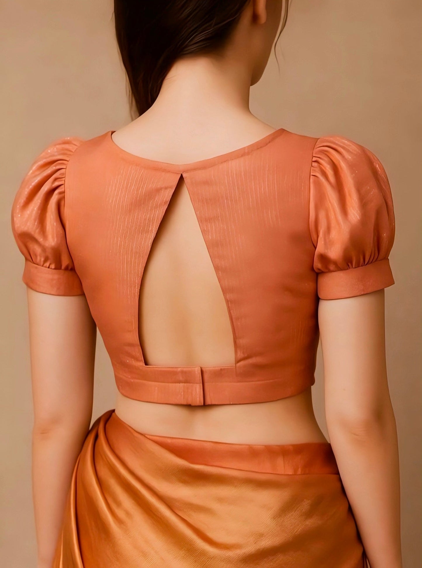 Woman wearing an orange blouse with open back on a beige background