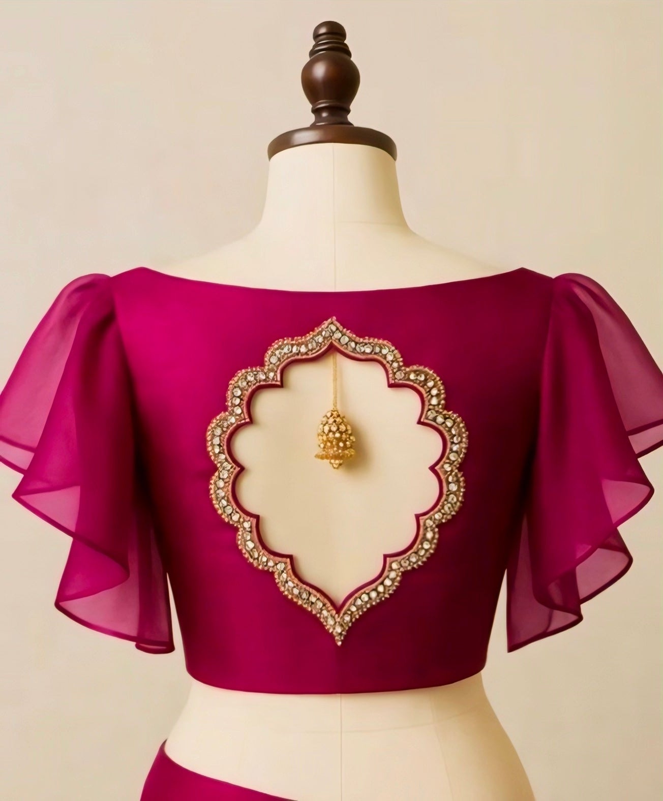 Magenta blouse with intricate gold embroidery on a mannequin against a beige background