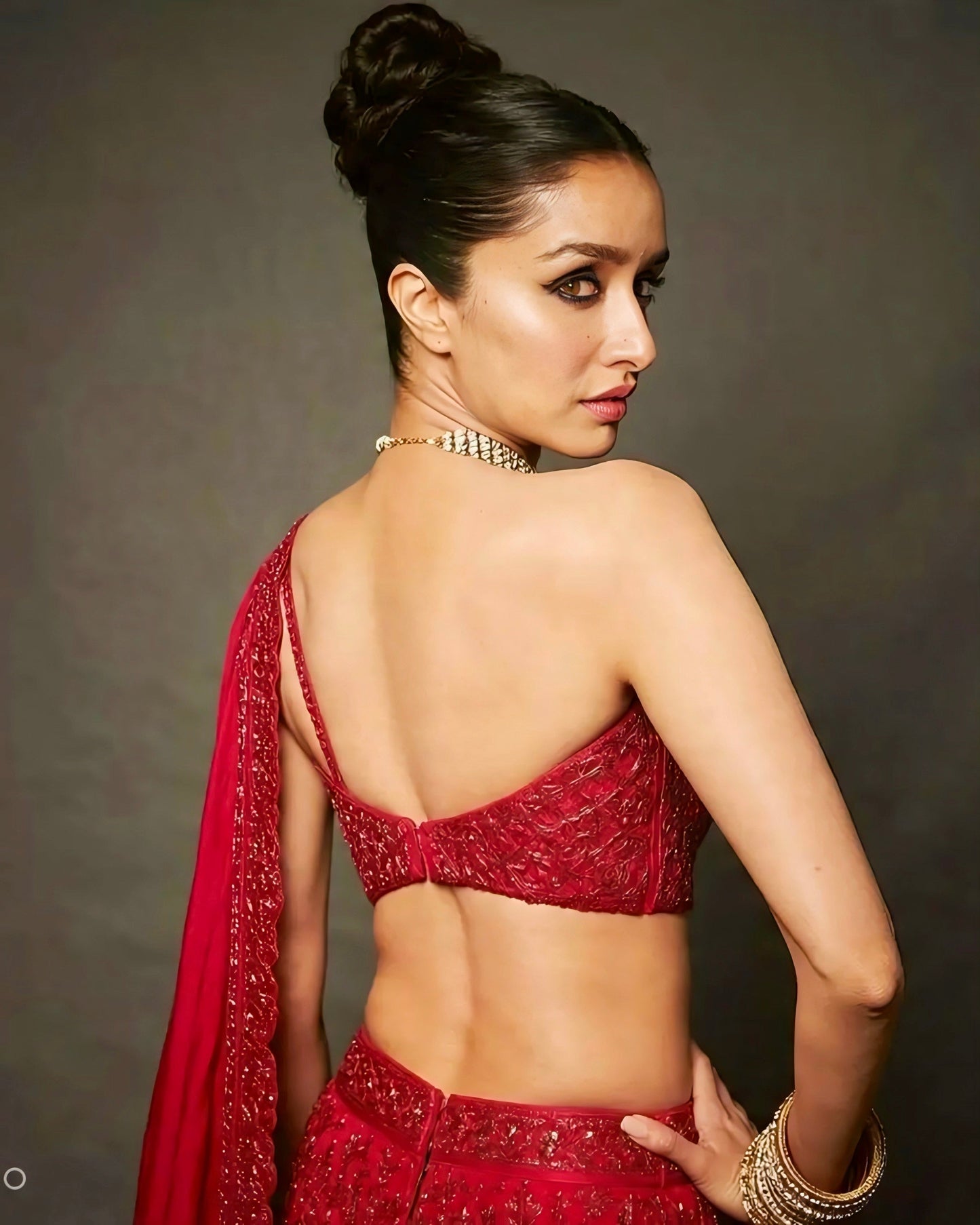 Woman wearing a red embroidered backless designer blouse with asymmetric strap style