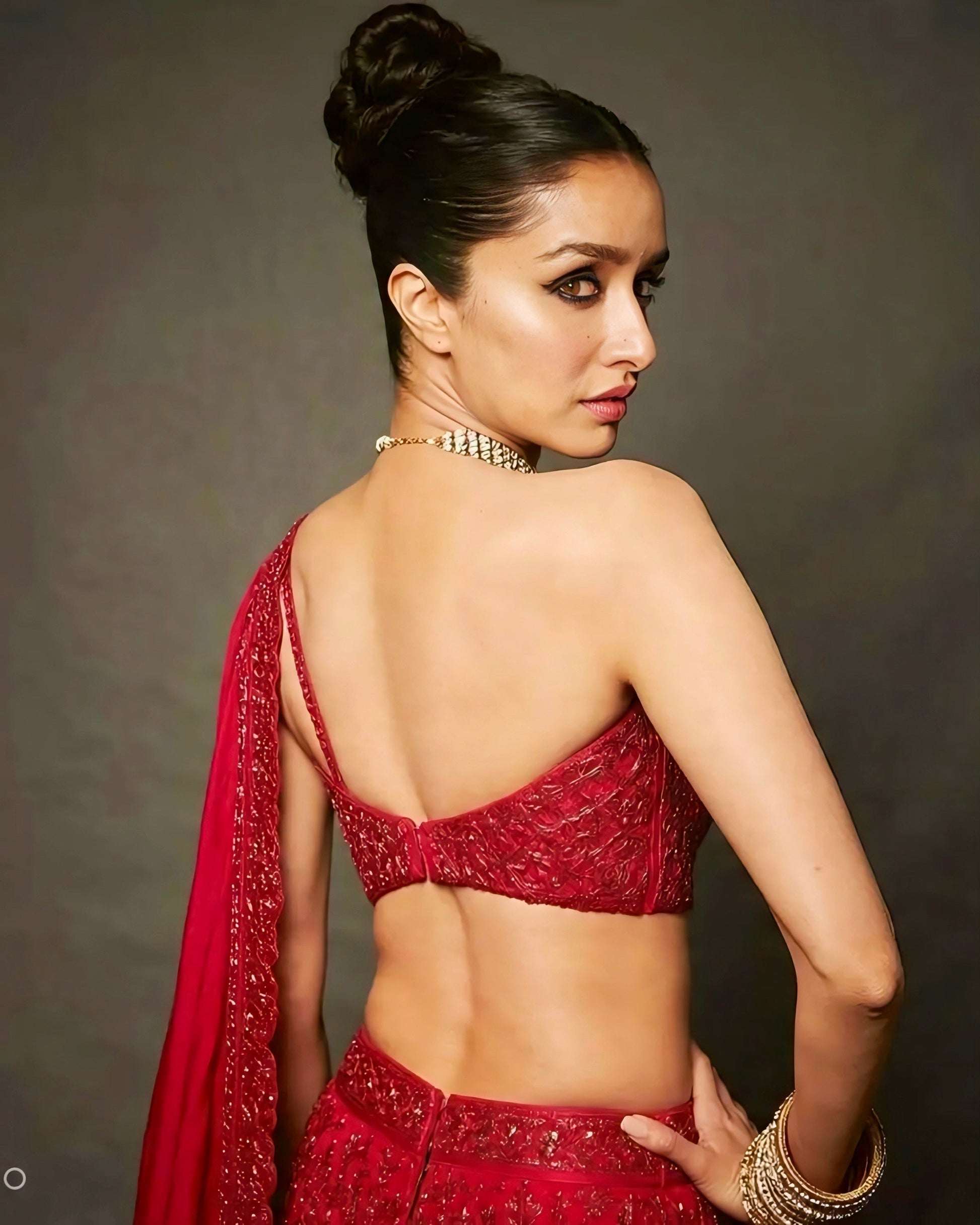 Woman wearing a red embroidered backless designer blouse with asymmetric strap style