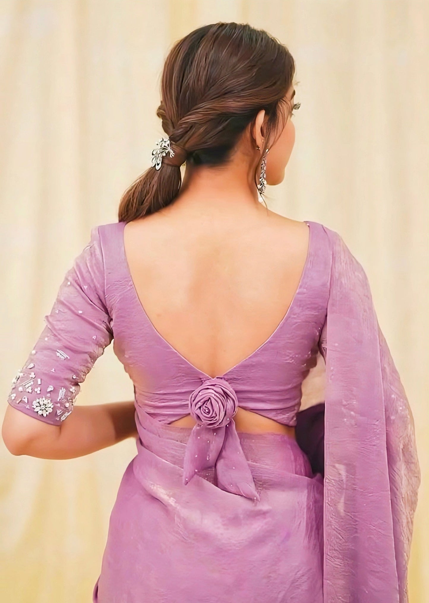 Woman wearing a lavender saree with a deep back neck blouse featuring a floral knot tie-up and embellished sleeves.
