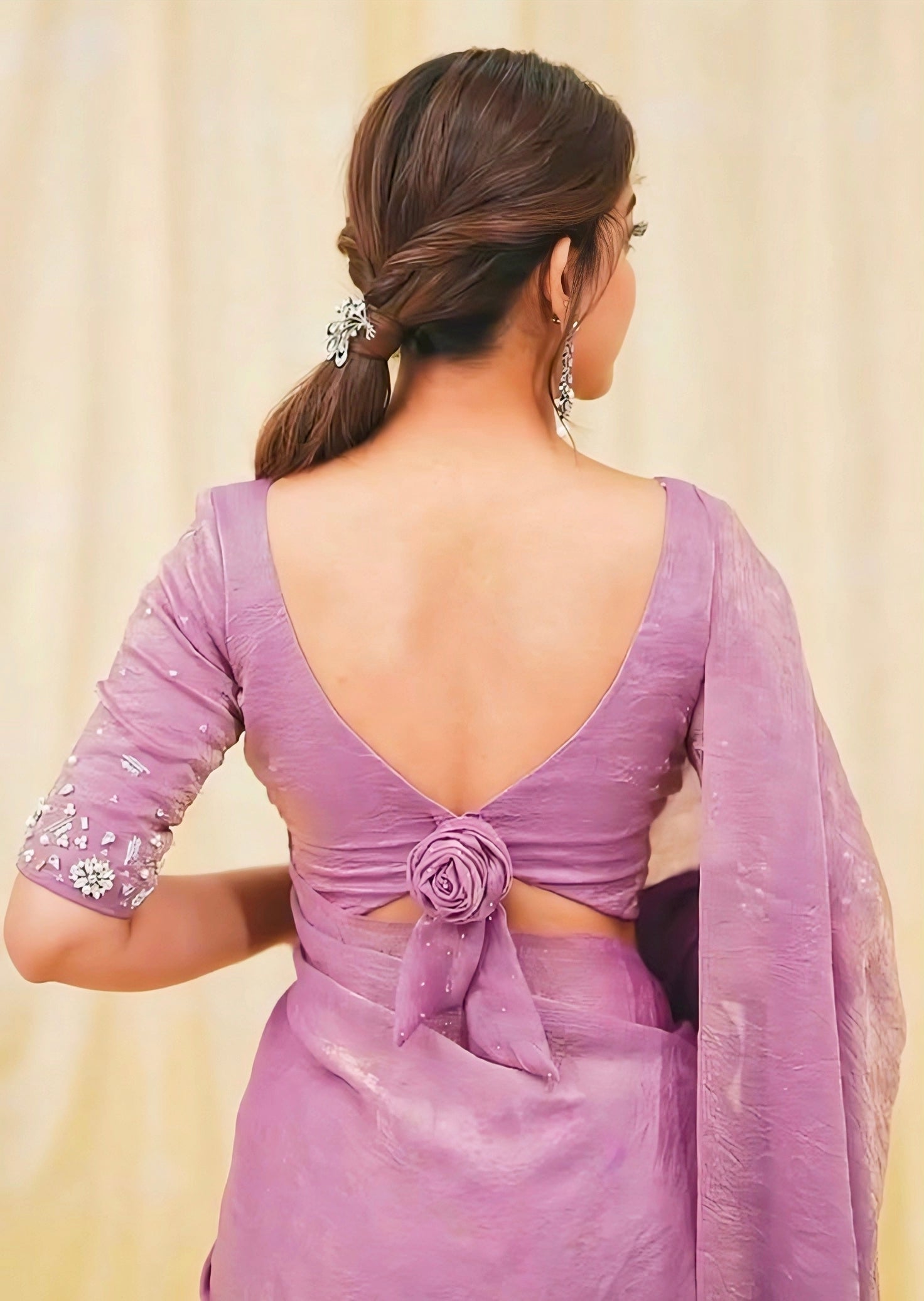 Woman wearing a lavender saree with a deep back neck blouse featuring a floral knot tie-up and embellished sleeves.