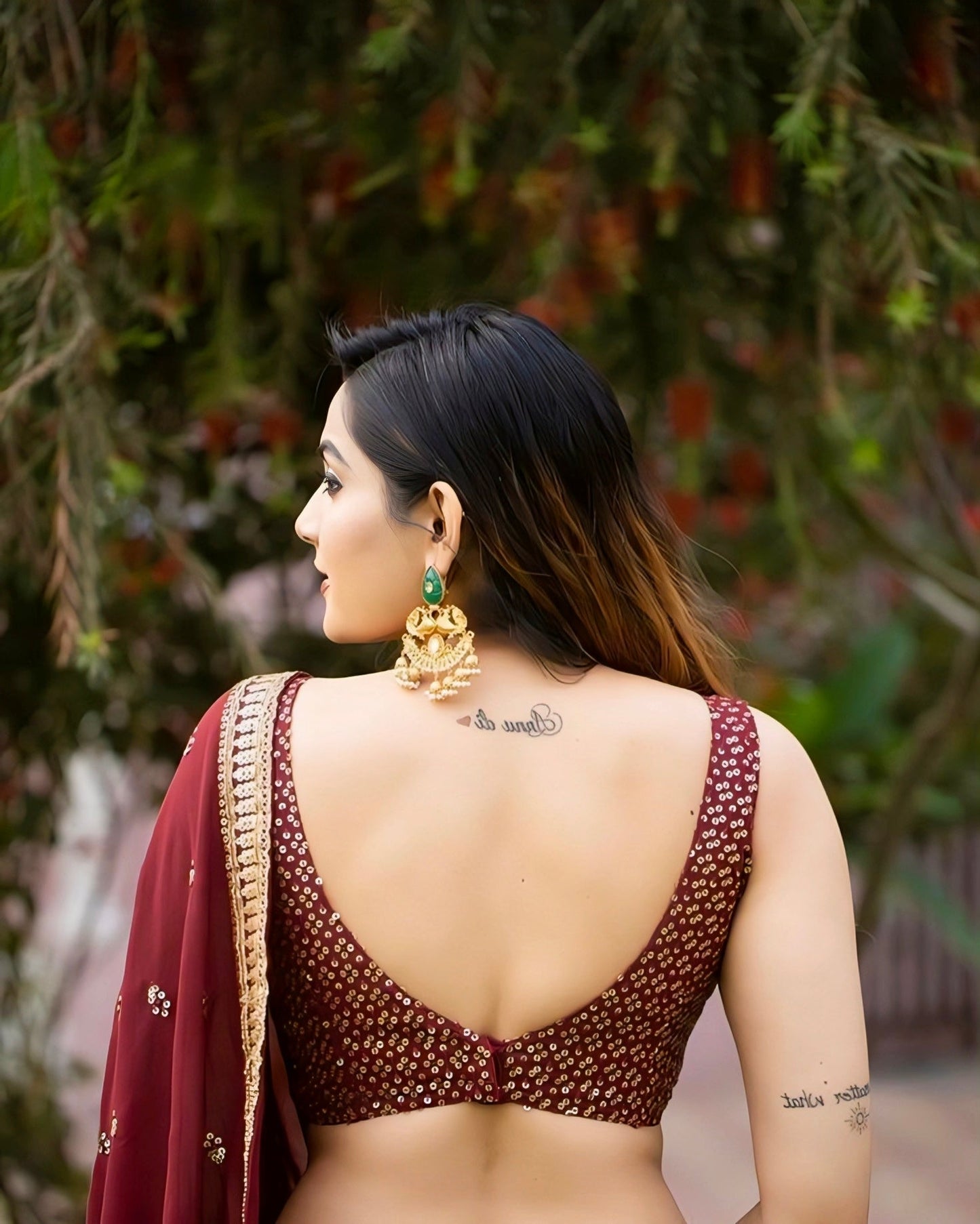 Woman wearing a maroon sequin backless saree blouse with deep V-cut design and traditional earrings, outdoor photoshoot