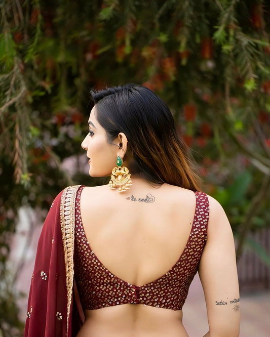 Woman wearing a maroon sequin backless saree blouse with deep V-cut design and traditional earrings, outdoor photoshoot