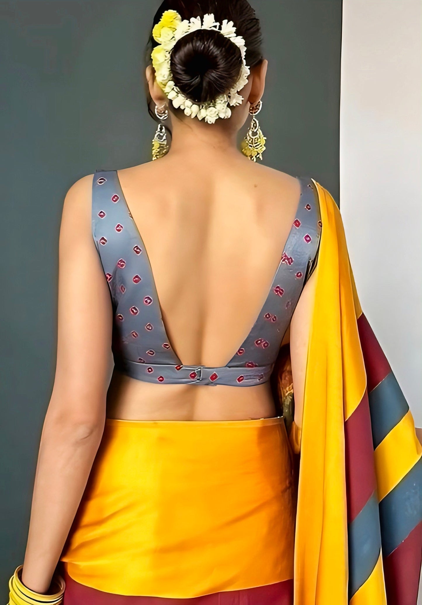 Woman wearing a deep V-back grey printed blouse paired with a vibrant yellow silk saree, styled with floral bun and traditional earrings.