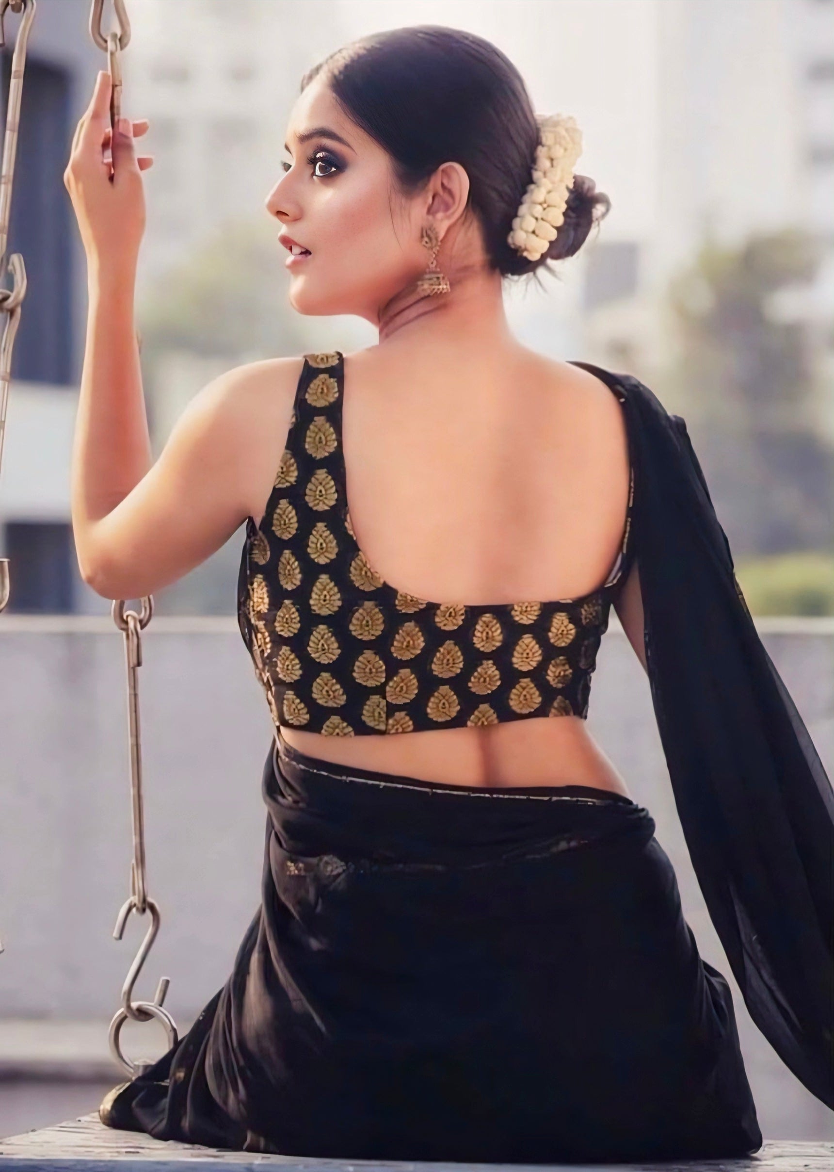 Black silk saree paired with a golden brocade deep-back blouse worn by a woman standing in a hallway — elegant traditional festive outfit.