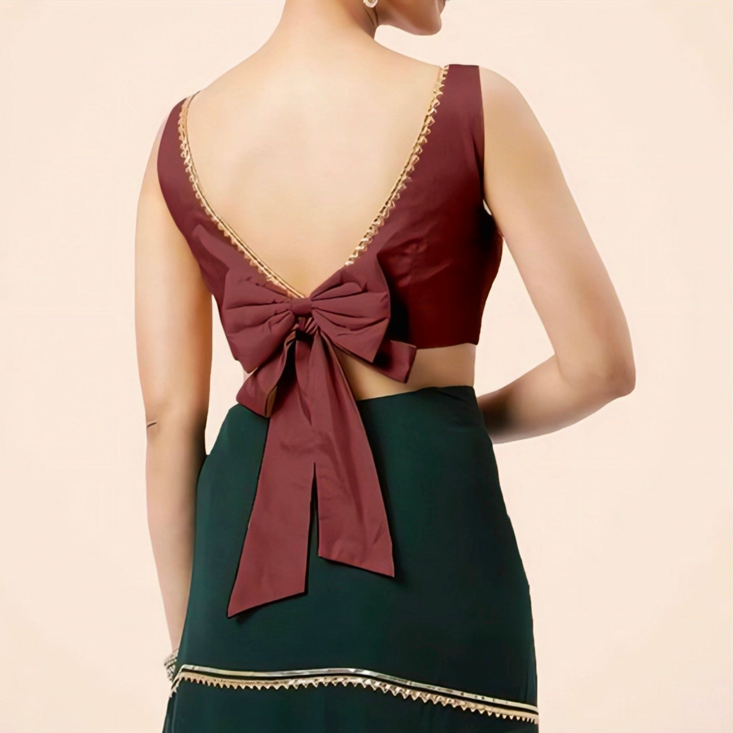 Woman wearing a maroon deep V-neck blouse with a large bow tie at the back, paired with a dark green lehenga.