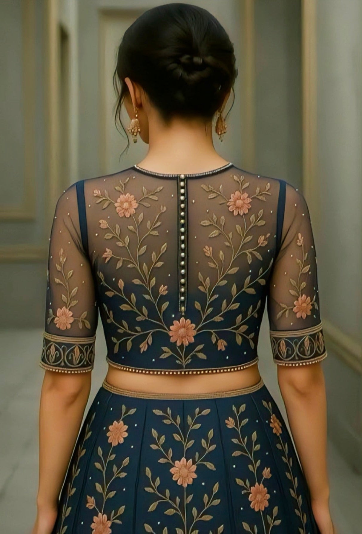 Woman wearing a navy blue net back blouse with floral embroidery and pearl-button detailing, matched with an embroidered lehenga.