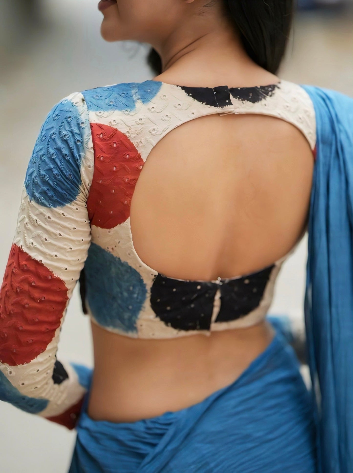Back view of a multicolor polka-pattern blouse with a large oval cut-out back design, paired with a blue saree.