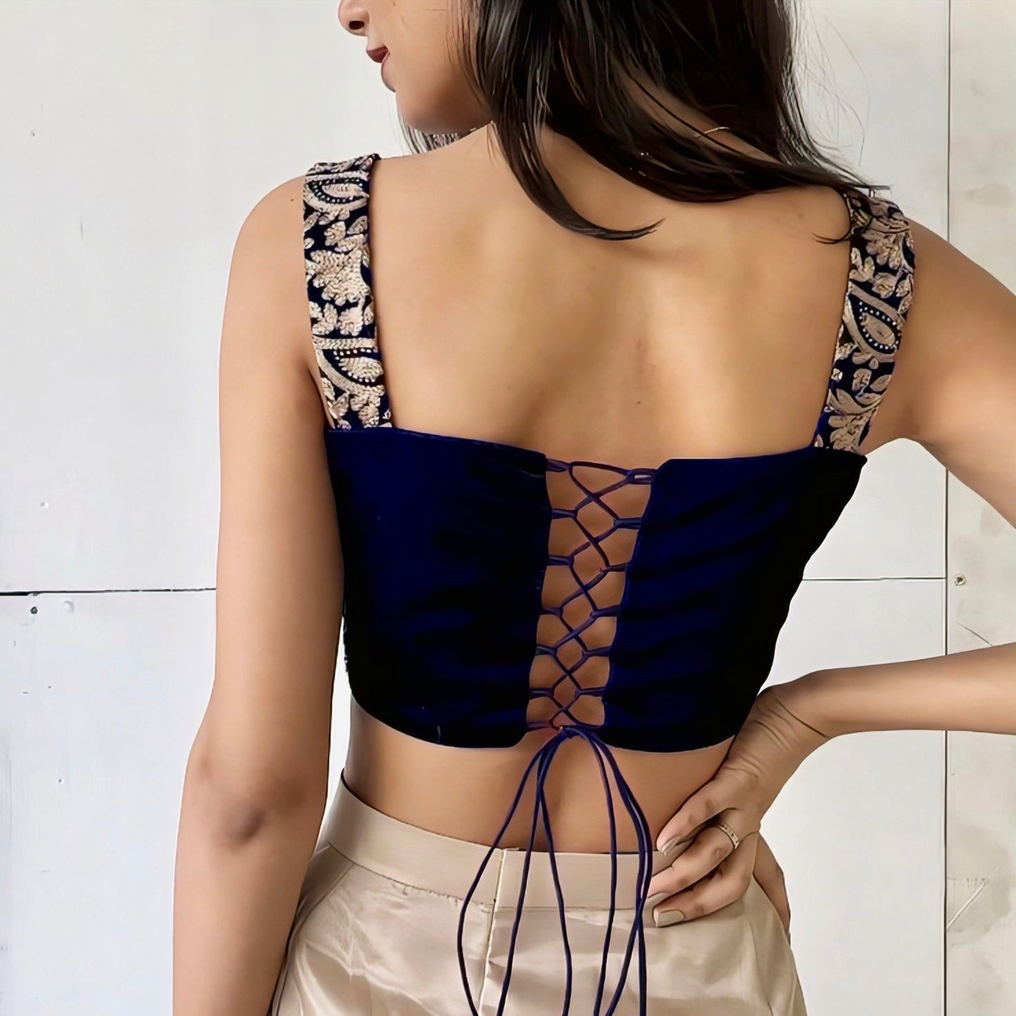 Woman wearing a navy blue embroidered sleeveless blouse with a lace-up back design and golden detailing.