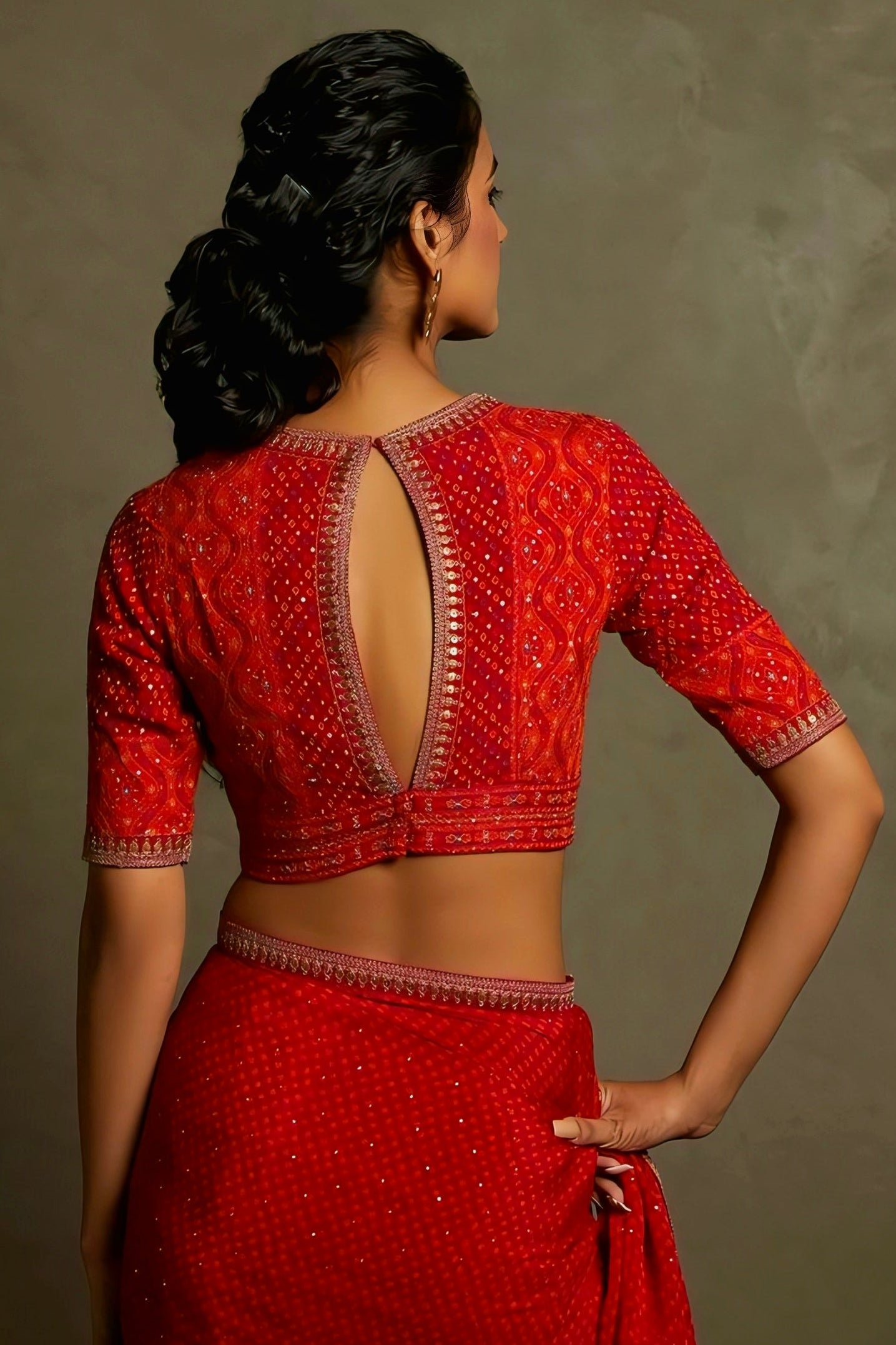 Woman wearing a red embroidered saree blouse with keyhole back neck design and zari border — traditional festive blouse style.
