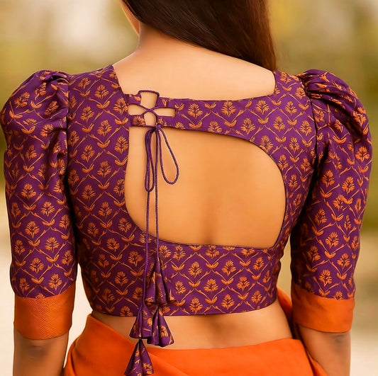Woman wearing a purple brocade saree blouse with puff sleeves, square back cut, and dori tie-up — traditional silk ethnic blouse design.