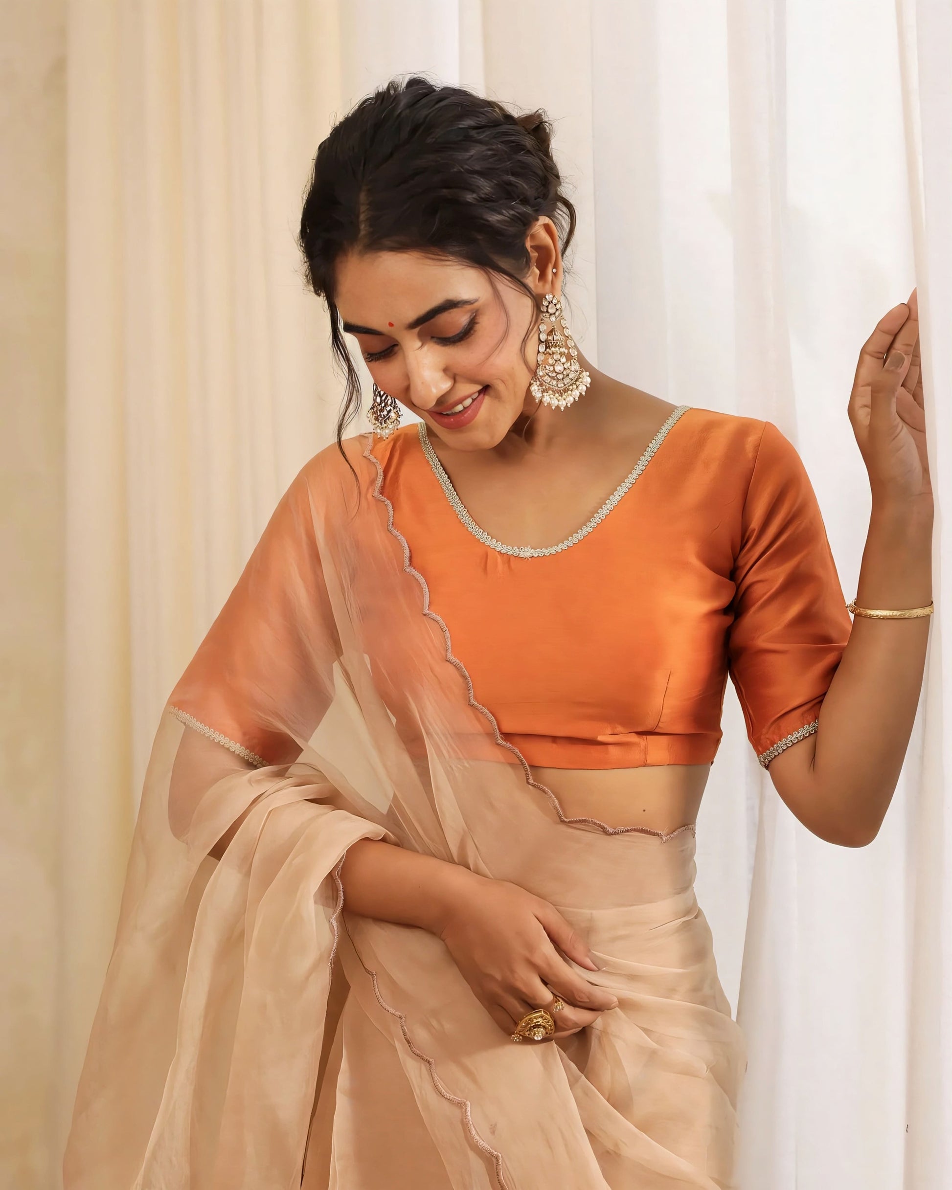 Burnt orange silk-look princess cut blouse with scoop neckline and elbow sleeves paired with a beige saree