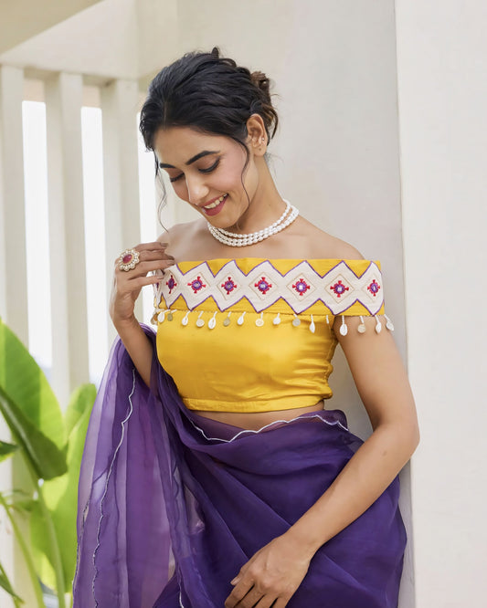 Mustard yellow princess cut off-shoulder blouse with embroidered neckline paired with a purple saree