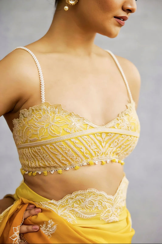 Yellow embroidered saree blouse with slim straps and lace detailing styled for festive wear.