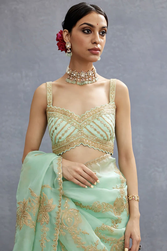 Mint green fancy blouse design with gold embroidery and scalloped neckline paired with a pastel saree.
