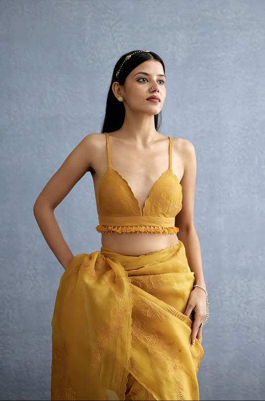 Mustard yellow haldi blouse design with deep neck and tassel detailing paired with saree