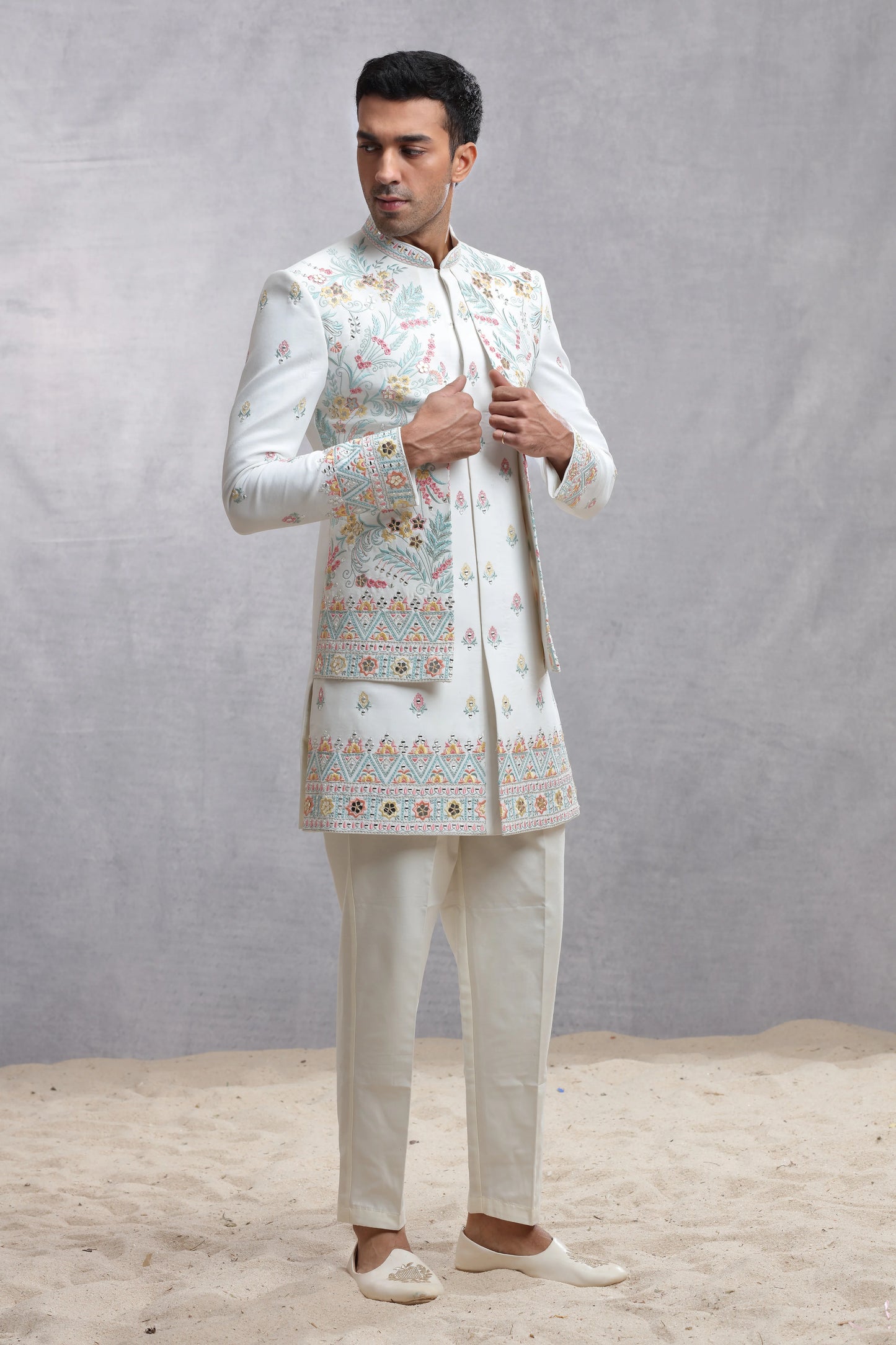 Man wearing elegant engagement white dress for men with pastel floral embroidery and matching trousers, styled for a modern groom look